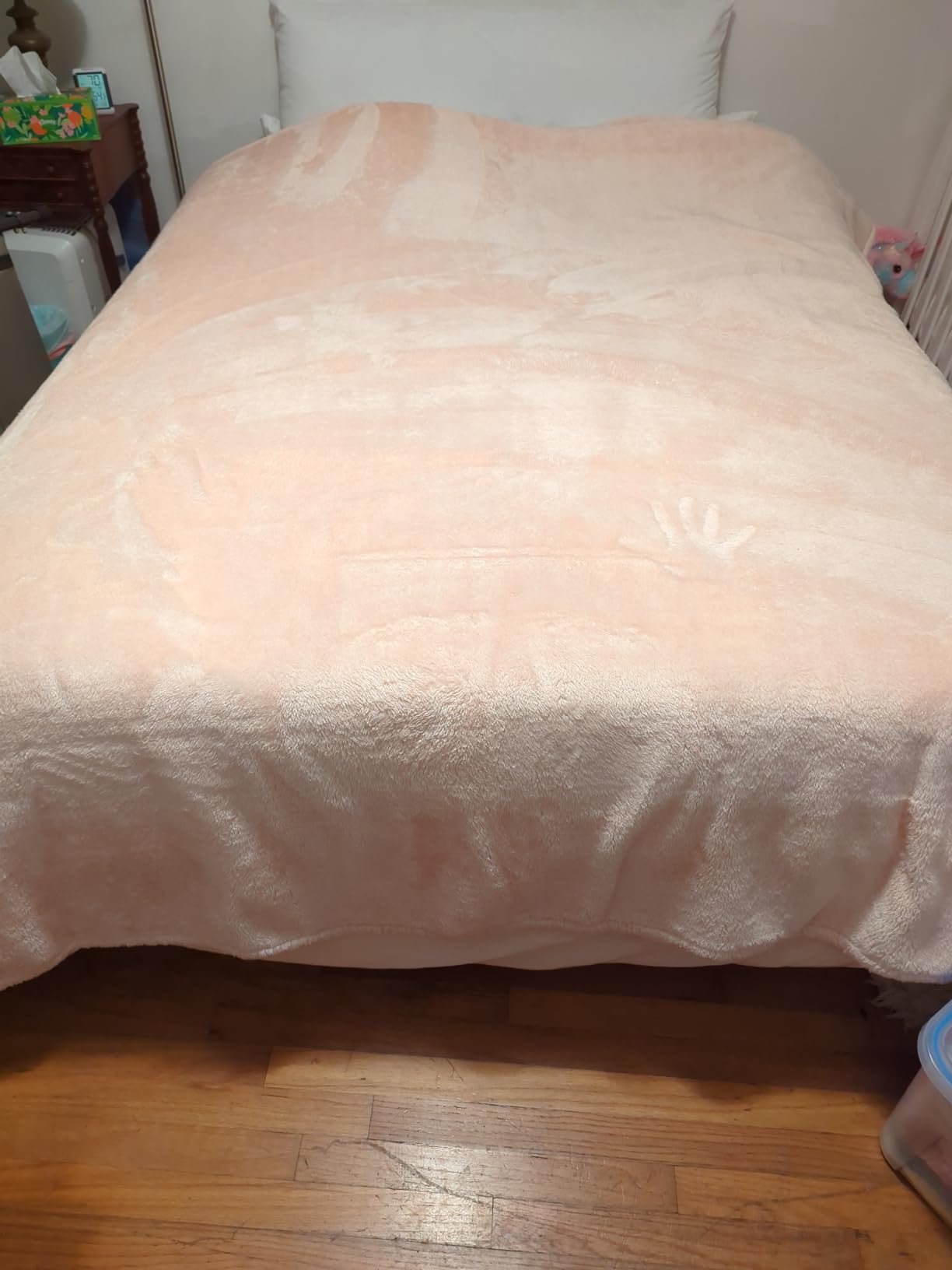 A blush plush Life Comfort blanket spread over a made bed, hanging past the mattress edge on both sides