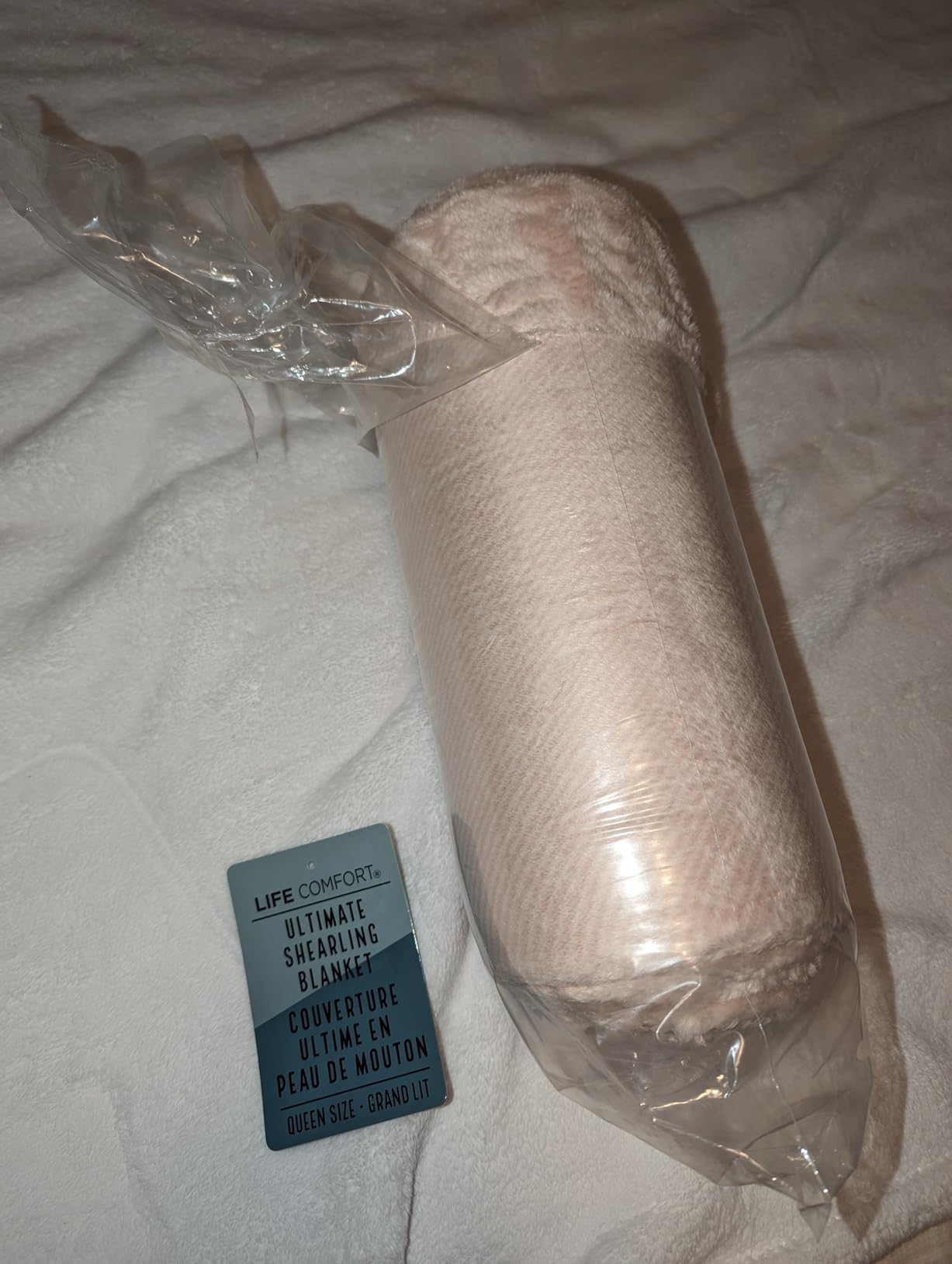 A queen size Life Comfort Ultimate Shearling Blanket in blush, rolled inside its clear bag with the hangtag beside it