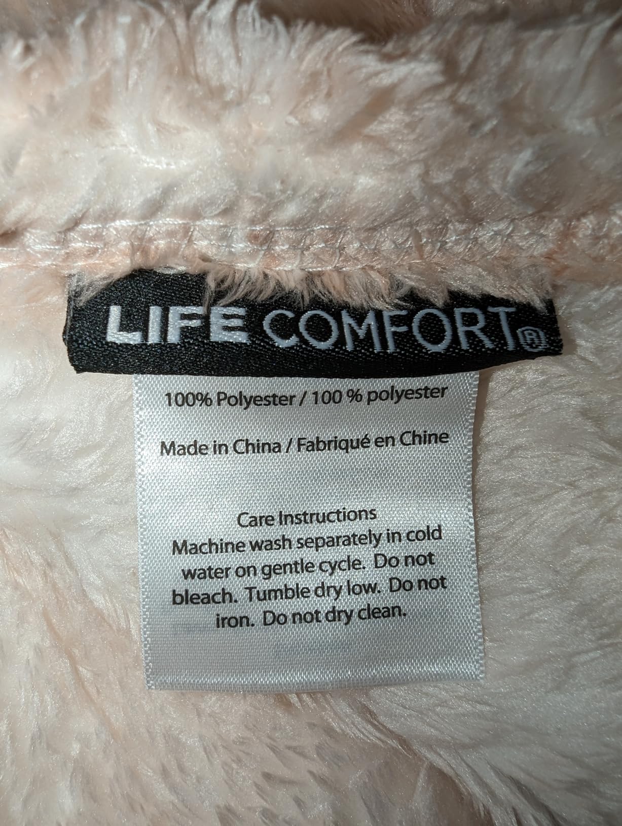 Close-up of the sewn-in Life Comfort care label on a cream shearling blanket, reading 100% polyester and cold gentle washing